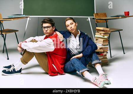 Two young people, a man and a woman, seated on the floor next to a school desk in a college classroom. Stock Photo