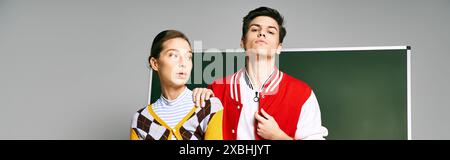 Two students, a man and a woman, dressed casually, standing together in front of a green board in a college classroom. Stock Photo