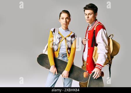 Two young individuals happily holding skateboards on a gray backdrop. Stock Photo