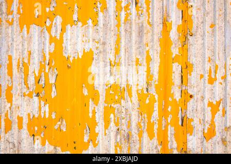 Close up of a weathered corrugated metal surface with peeling yellow paint, revealing rust and wear underneath. Stock Photo