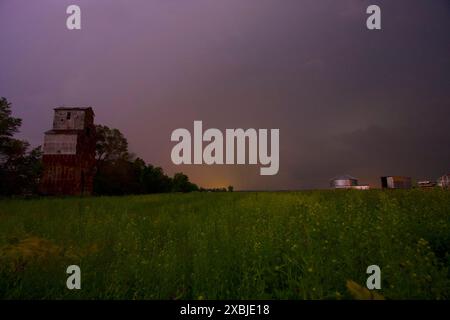 Old grain mill in a lush meadow, illuminated by lightning at night. Stock Photo