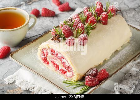 Raspberry sponge roll with jam, fresh berries, cream cheese covered with white chocolate close-up in a plate on the table. Horizontal Stock Photo