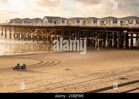 People sitting on beach in golden evening light near Crystal Pier with over water beach cottages at Pacific Beach San Diego Southern California USA Stock Photo