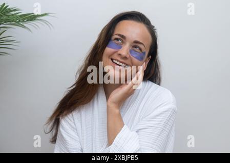 Dreaming brunette woman with under-eye patches smiling on light background portrait pretty lady Stock Photo