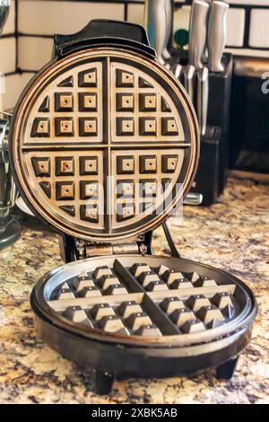 A well-loved electric waffle iron with its lid open on a kitchen counter. Stock Photo