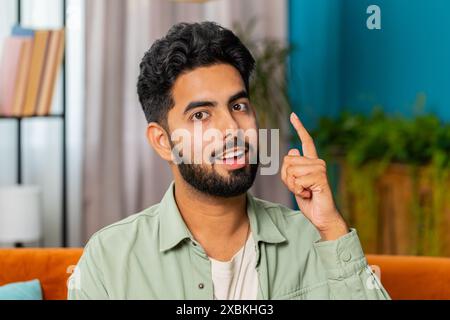 Eureka. Thoughtful clever inspired Indian man make gesture raises finger came up with creative plan feels excited with good idea inspiration motivation, question at home apartment. Guy sits on couch Stock Photo