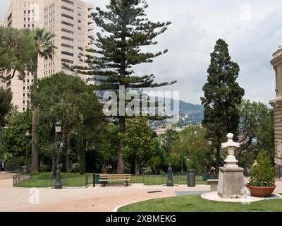 Green park with scattered trees, benches and tall buildings in the background under a cloudy sky, monte carlo, monaco, france Stock Photo