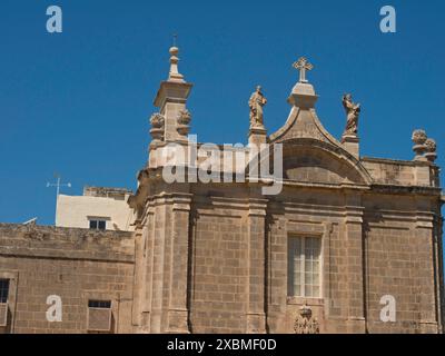 Stone church building with statues and cross on the roof, blue sky in the background, gozo, mediterranean sea, malta Stock Photo