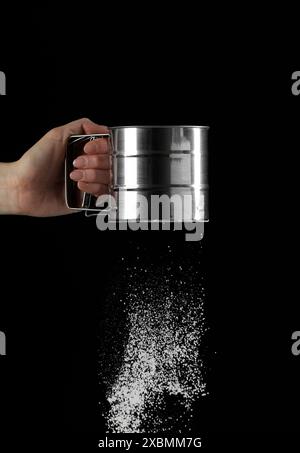 Woman sieving flour against black background, closeup. Space for text ...