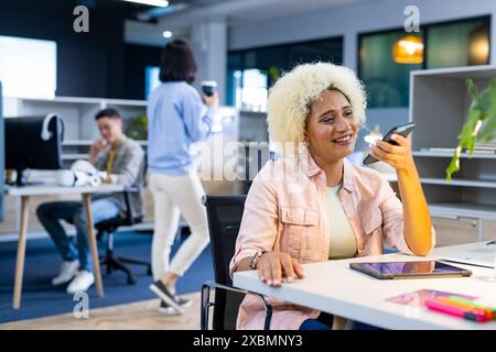 Biracial woman smiling while talking on smartphone in modern business office Stock Photo