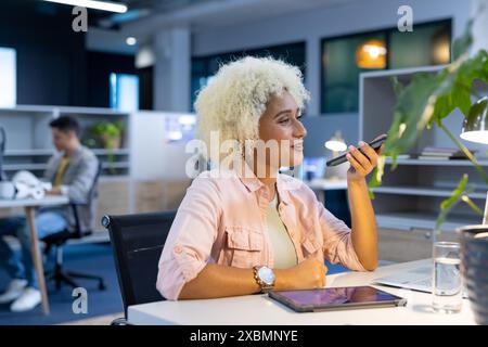 Biracial woman using smartphone in modern office for business Stock Photo