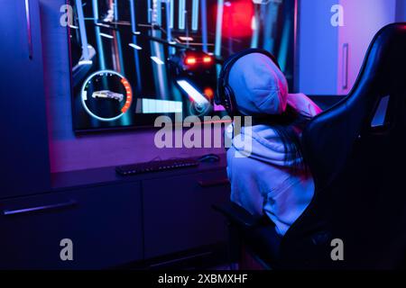 Happy biracial woman in headphones and hoodie, playing a video games on a large screen, copy space Stock Photo