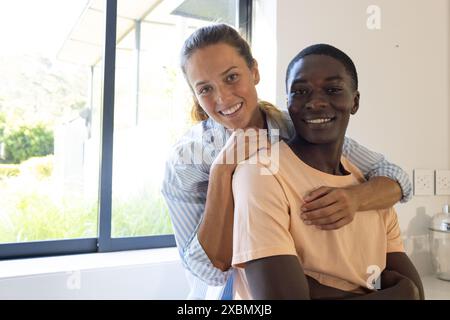 A diverse couple smiles, woman resting her hands on the man's shoulders, copy space, at home Stock Photo