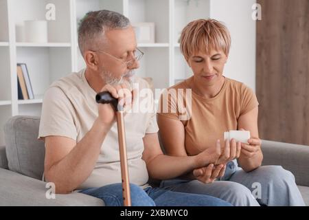 Mature woman giving pills to her sick husband with stick at home Stock Photo