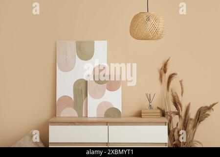 Chest of drawers, pampas grass, lamp and beautiful pictures on beige wall in room Stock Photo