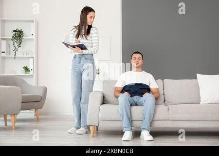 Female psychologist with notebook and hypnotized young man in office Stock Photo