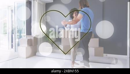 Image of yellow neon heart and white spots over happy diverse couple dancing among packing boxes Stock Photo