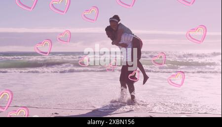 Image of pink hearts over happy african american couple piggybacking on beach Stock Photo