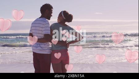 Image of pink hearts over happy african american couple embracing on beach Stock Photo