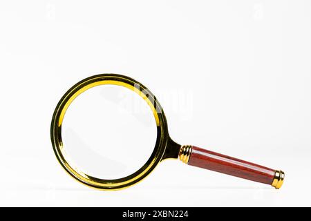 A magnifying glass with a wooden handle is shown on a white background. Concept of curiosity and exploration, as the magnifying glass is often used to Stock Photo