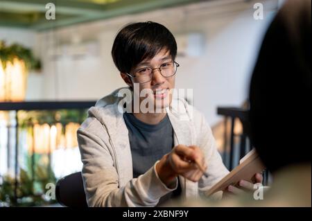 A young, smart Asian male college student is tutoring, helping his friend with math homework, discussing a co-project, or preparing for an exam togeth Stock Photo