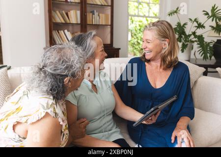 Diverse group of senior women friends using tablet at home on sofa Stock Photo