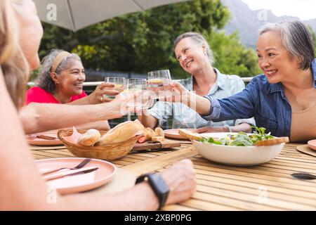Group of diverse senior women enjoying drinks and food together at outdoor table Stock Photo