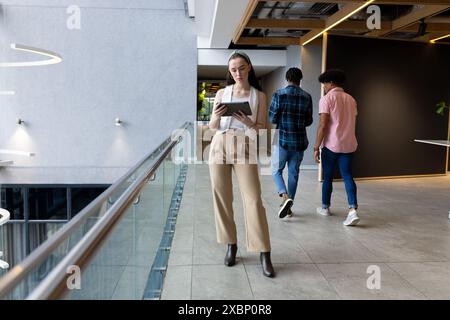 Caucasian woman using tablet in office hallway for business collaboration, copy space Stock Photo