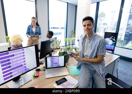 biracial man in modern office using smartphone, collaborating with colleagues Stock Photo