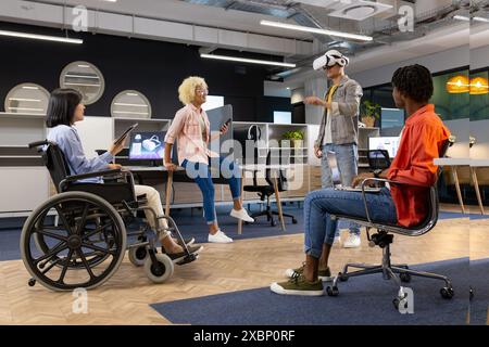 Business colleagues in office watching man using vr headset, asian woman in wheelchair, inclusivity Stock Photo