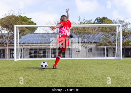 African American soccer player kicking soccer ball on field, appearing strong and fit Stock Photo