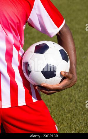 African American soccer player holding soccer ball in red and white sports uniform Stock Photo