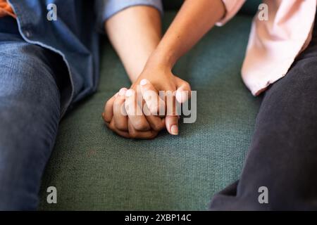 Diverse couple holding hands on green couch, showing affection Stock Photo