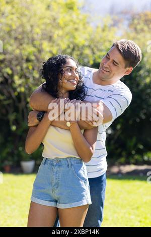 Young Caucasian man hugging young Asian woman from behind, both smiling warmly Stock Photo