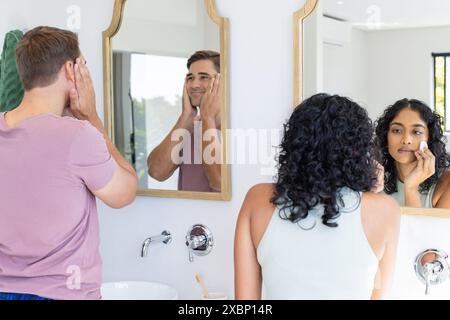 Diverse couple getting ready in front of bathroom mirrors Stock Photo