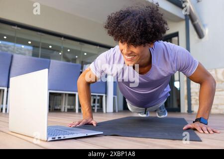 Biracial, Fit man exercising doing push-ups, focused on laptop screen, looking strong and fit Stock Photo