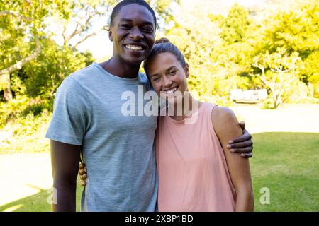 Happy diverse couple smiling and embracing outdoors in a sunny garden Stock Photo