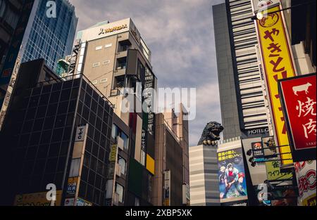 Urban scene in Shinjuku, Tokyo featuring the iconic Godzilla head on a building amidst modern architecture and vibrant signage Stock Photo