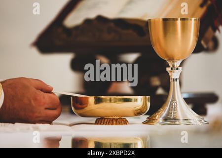 Golden chalice and paten standing on altar with priest holding the paten during a mass celebration in a church Stock Photo