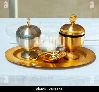 Golden and silver chalices and a golden shell with holy water for the sacrament of baptism during a church ceremony Stock Photo