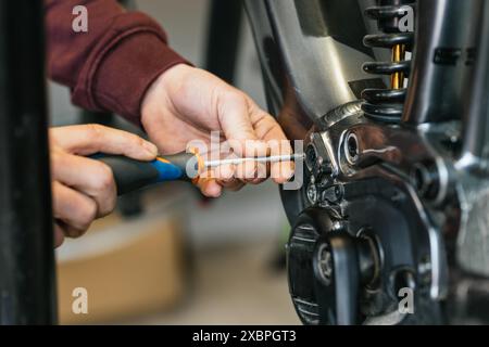 Detail shot of the hands of a bike mechanic using a screwdriver to manipulate and unscrew the electrical system of an electric mountain bike. Stock Photo