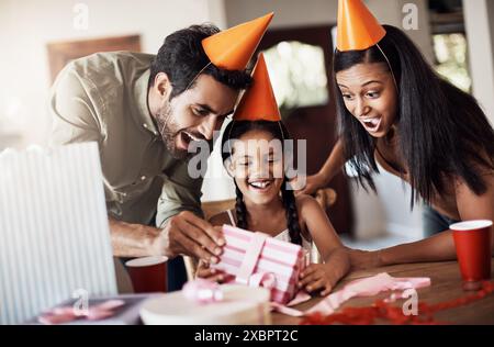 Parents, child and wow in home for birthday gift in table with party hat and fun. People, family and happy or excited for present with love, care and Stock Photo