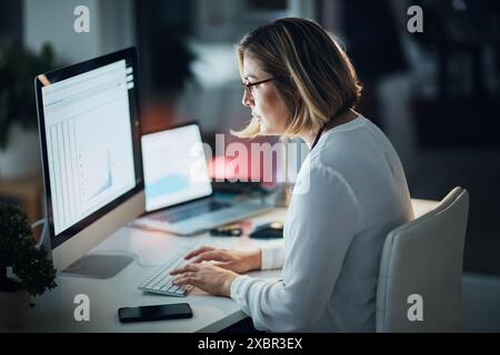 Computer screen, night and business woman with data analytics, spreadsheet and statistics report for deadline. Tech analyst in office with graphs Stock Photo