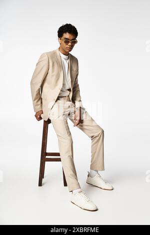 Handsome African American man in tan suit sitting on stool with stylish sunglasses. Stock Photo