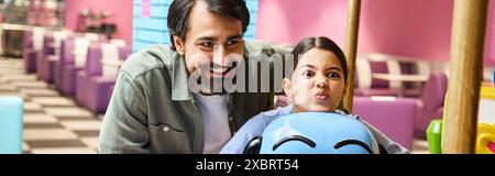A father and child happily sitting on a toy in a childrens play area inside a mall during the weekend. Stock Photo