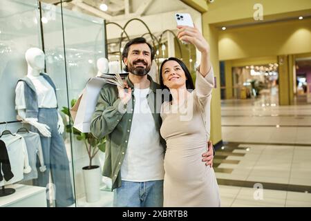 A joyful couple, amid a bustling shopping mall, embraces for a selfie, capturing their shared moments of happiness. Stock Photo