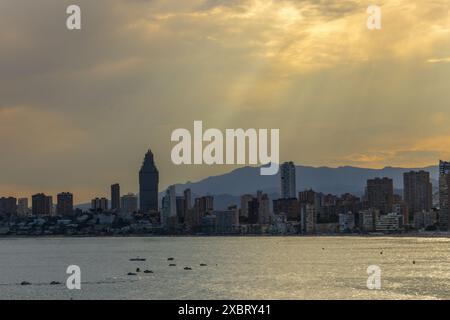 The image depicts a coastal cityscape of Benidorm, Spain, with a view of the sea. The skyline is characterized by modern high-rise buildings. Stock Photo