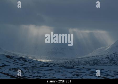 Sunlight streaming through clouds over snowy mountains Stock Photo