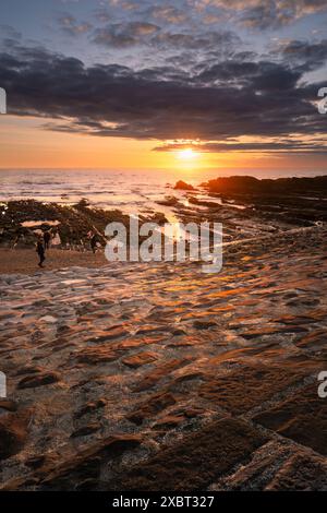 An intense sunset over people walking along Breakwater beach on the coast of Bude in Cornwall in the UK. Stock Photo