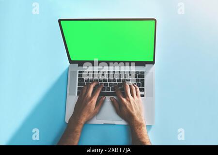 Green screen, laptop and hands of man in studio top view for social media, email or online communication on blue background. Mockup, keyboard and Stock Photo